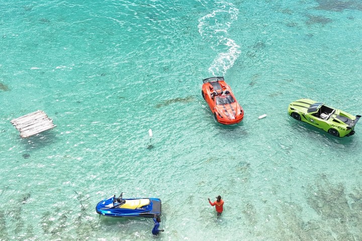 Two people with jet skis and car-shaped boats on clear turquoise water.